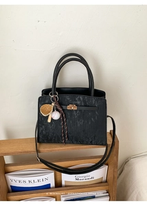 Détail du sac noir texturé avec fermoir en métal doré sur une étagère en bois