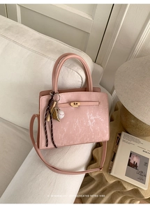 Détail d'un sac seau vintage rose avec texture verticale et breloque baseball sur un canapé