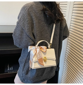 Detailed shot of white leather crossbody bag with gold buckle and decorative silk scarf
