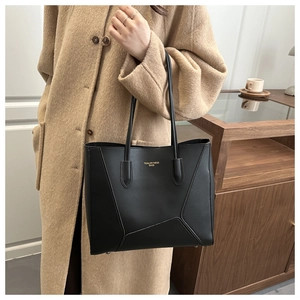 Detail of black tote bag with geometric stitching and gold logo on wool coat