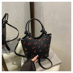 Detail of black tote bag with red cherry print featuring a knotted handle and shoulder strap
