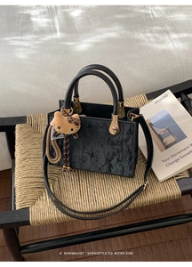 Détail d'un sac à main carré noir avec pendentif peluche Hello Kitty sur chaise