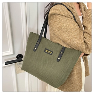 Detail of dark green corduroy tote bag with black leather straps and gold metal rivets