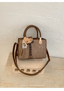 Détail d'un sac à main marron texturé avec breloque Hello Kitty sur socle en pierre