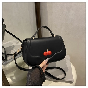 Détail du sac à bandoulière en similicuir noir avec boucle cerise rouge et sangle