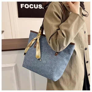 Detail of denim tote bag with brown leather handles and a decorative printed silk scarf