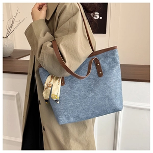 Detail of denim blue tote bag with brown leather handles and decorative silk scarf