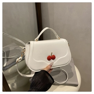 Détail d'un sac à bandoulière blanc avec cerises rouges en 3D et finition mate
