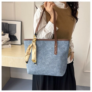 Detail of blue textured tote bag with brown leather handles and a yellow floral silk scarf