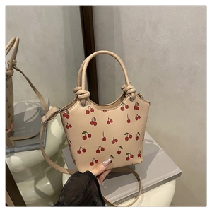 Detailed view of beige bucket bag with cherry print and knotted handle design