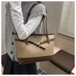 Close-up of beige and brown leather tote bag worn on shoulder in a modern setting
