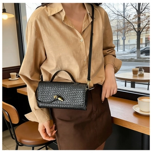 Detail of black woven texture handbag with golden twist lock on a crossbody baguette bag
