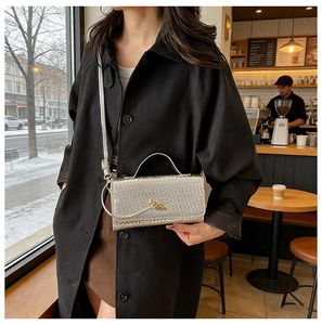 Close-up of silver woven leather bag with gold knot clasp and textured detail