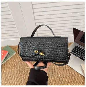 Detail of black woven leather handbag featuring a decorative gold metal knot twist lock