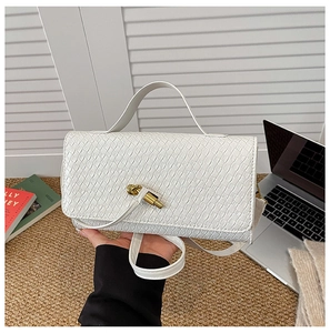 Close-up of woven texture and golden knot clasp on a white leather baguette handbag