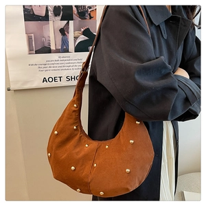 Detail der dunkelbraunen Wildleder-Halbmondtasche mit Goldnieten getragen von einem Model