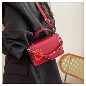 Detail van rode lederen crossbodytas met gouden gesp gedragen met een zwarte blazer