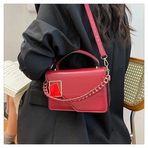 Detail van rode leren crossbodytas met gouden gesp en kettingriem op een zwart pak