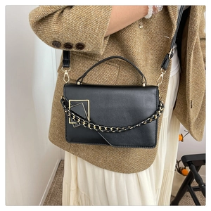 Detail van de zwarte leren tas met gouden gesp en kettingriem gedragen door een model