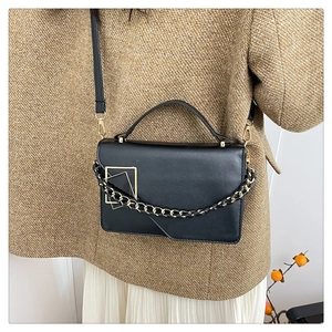 Detailopname van zwarte leren crossbodytas met gouden hardware op de outfit van een model