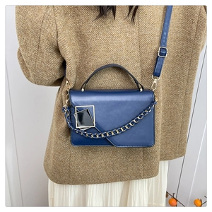 Detailopname van een marineblauwe matte handtas met gouden ketting op tweed jasje
