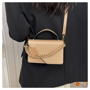 Detail van kaki lederen handtas met gouden ketting gedragen op een zwart kostuum