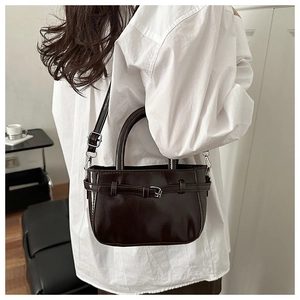 Detail of dark brown patent leather handbag with glossy finish and metal strap buckle