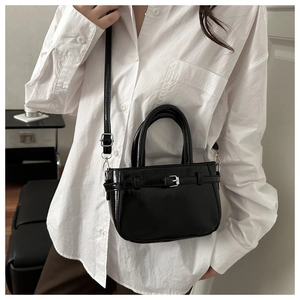 Close-up of black glossy crossbody bag with decorative silver buckle and leather strap detail