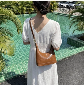 Detail of brown glossy leather shoulder bag with embossed texture worn with white dress