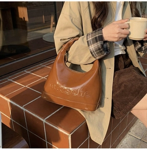 Brown glossy leather hobo bag with embossed logo shown in a lifestyle cafe setting