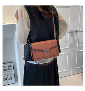 Detail of a brown vintage leather crossbody bag with a silver cross buckle and chain