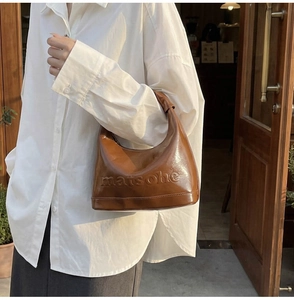 Detail of brown patent leather hobo bag with embossed lettering on textured surface