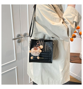 Detail of black woven bucket bag with gold logo and cute plush bear charm accessory