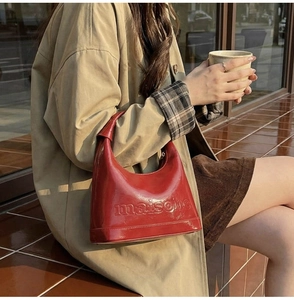 Glossy red patent leather shoulder bag with maison embossing held by model in trench coat