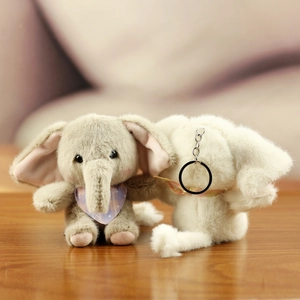 Close-up of plush elephant keychain set in grey and cream with soft wood background