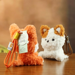 Detail van pluche puppy-hangers in oranje en wit met geweven bandjes op houten oppervlak
