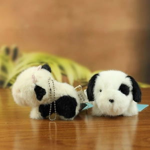 Close-up of black and white plush animal keychains with silver chains on a wooden desk