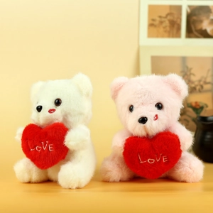 Detail view of plush teddy bears in white and pink holding embroidered LOVE hearts