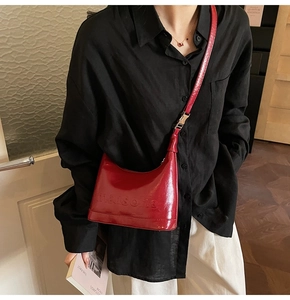 Detail of red glossy leather handbag featuring embossed lettering and metal strap buckle