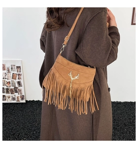 Détail du sac bandoulière en daim marron avec de longues franges et emblème de cerf doré