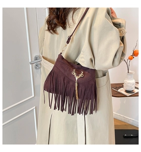 Détail d'un sac en daim marron foncé avec de longues franges et un cerf doré