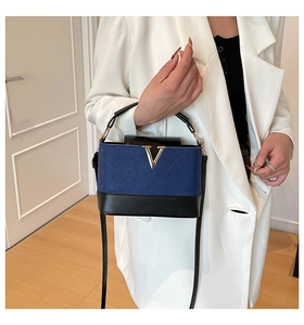 Detail showing contrast blue suede textures and gold V-shaped metal hardware on the handbag