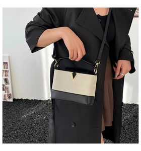 Detail der Kontrasttasche mit Steppmuster, V-förmigem Goldlogo und oberem Griff
