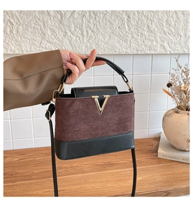 Detail der zweifarbigen matten Handtasche mit goldenem V-Logo auf Holztisch