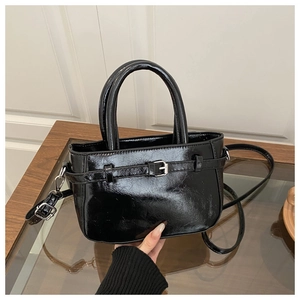 Detail of glossy black handbag featuring cylindrical handles and decorative buckle design
