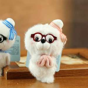 Close-up of plush seal keychain with red glasses and pink bow detail on wood background