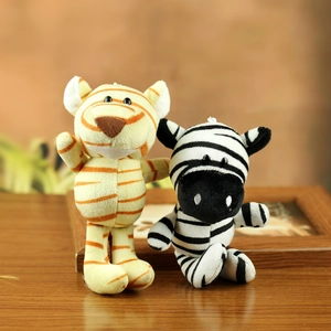 Cute plush tiger and zebra keychain charms on a wooden desk in a warm home setting