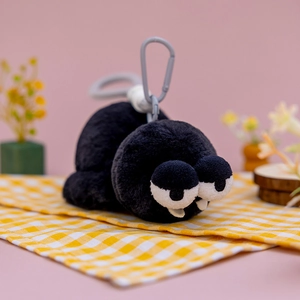 Dettaglio del ciondolo mostro di peluche nero con grandi occhi e zanne su panno a quadretti