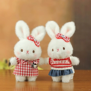 Close-up of cute plush bunny charms in red plaid and striped outfits on wood