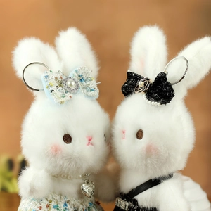 Detail of two plush white rabbit keychains with tweed bows and metallic heart charms